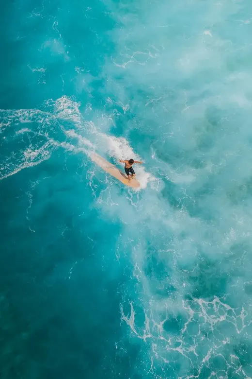 Surfer on a turquoise wave from above
